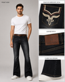 A man modeling dark wash flare jeans with a white t-shirt and white sneakers, shown alongside three detail close-ups highlighting the embroidered back pocket, leather patch, and flared leg opening.