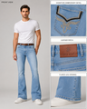 A man modeling light-wash blue jeans with a white t-shirt and white sneakers on a light gray studio background. The image includes three detail callouts on the right showing the back pocket embroidery, a brown leather patch with 'ONE MAN' branding, and the flared leg opening.