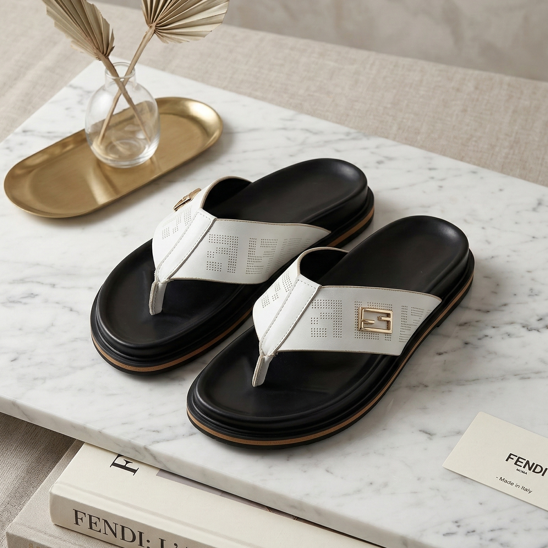 Black and white sandals on a marble surface with Fendi books and decorative items.