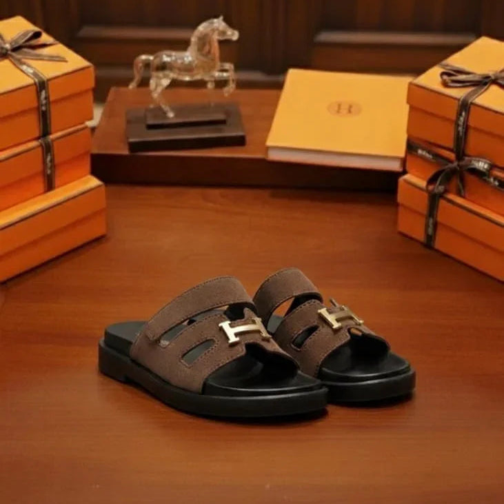 Brown sandals with gold buckles on a wooden surface with 'UNIVERSES' branding.