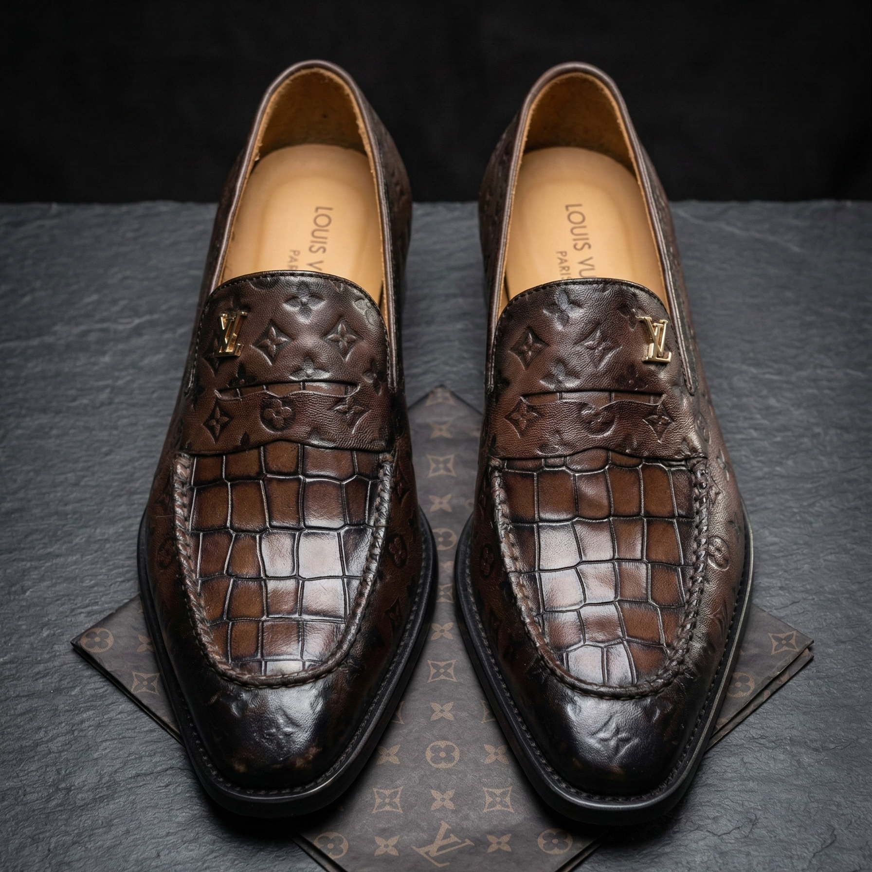 Pair of brown leather loafers on a dark surface with a brand logo.