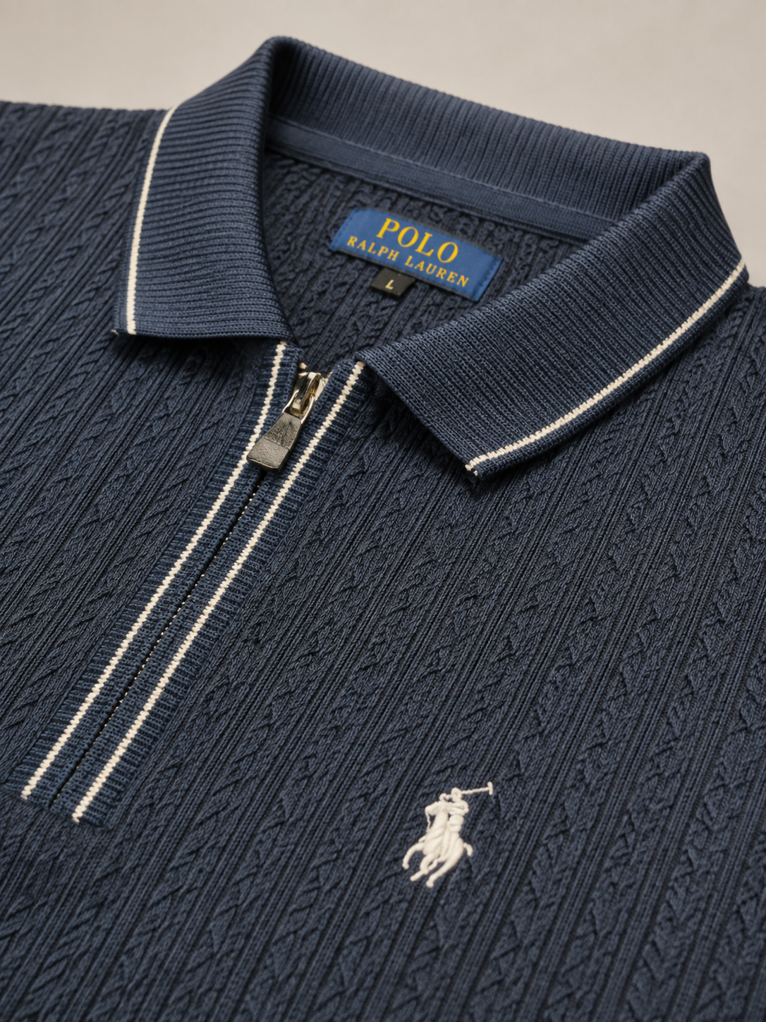 Close-up of a navy blue Polo Ralph Lauren knit zip-up polo shirt with a white embroidered pony logo and white contrast stitching.