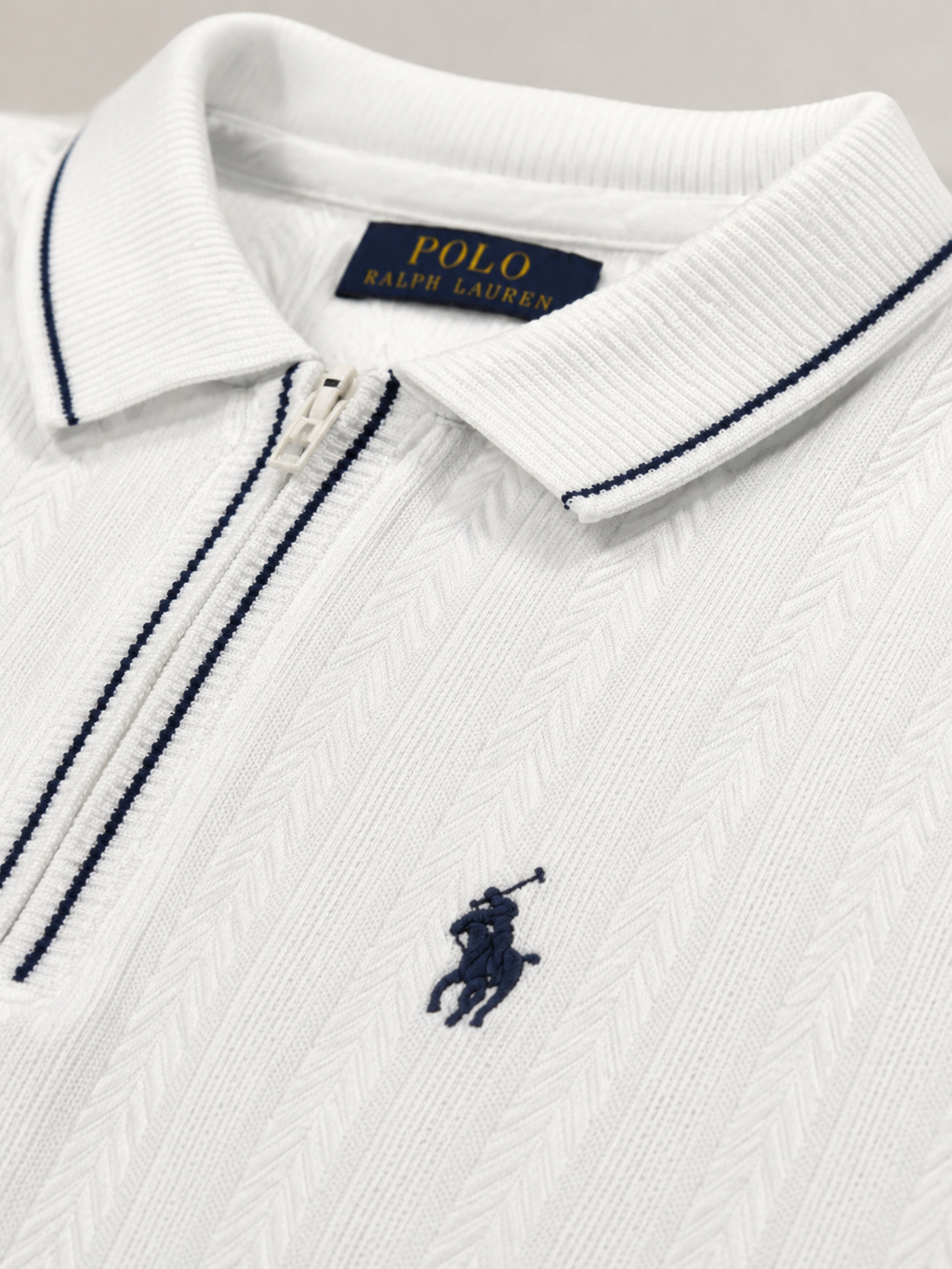 Close-up of a white Polo Ralph Lauren zip-up polo shirt with navy blue piping and the signature embroidered polo player logo on the chest.