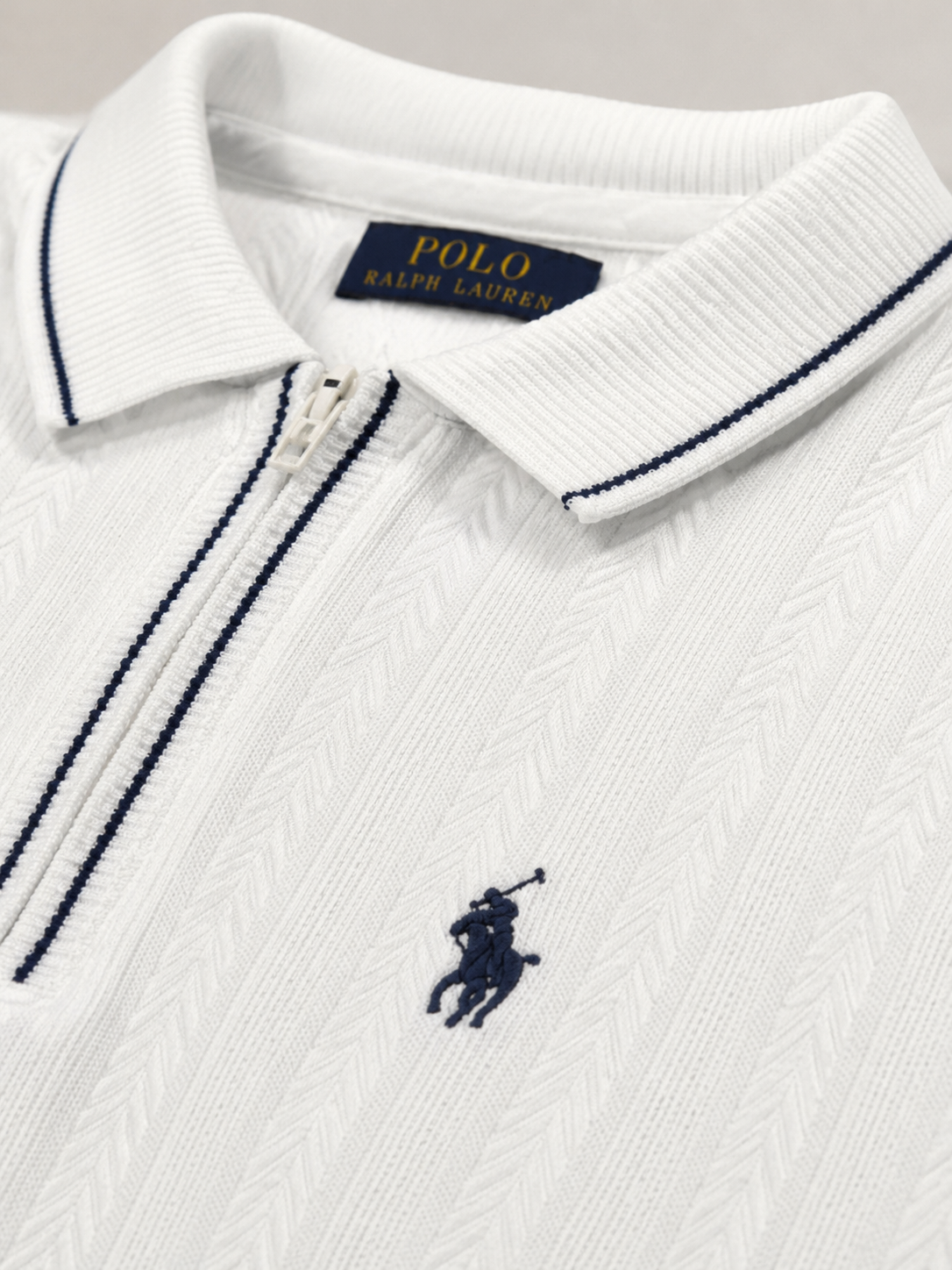Close-up of a white Polo Ralph Lauren zip-up polo shirt with navy blue piping and the signature embroidered polo player logo on the chest.