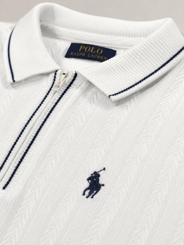 Close-up of a white Polo Ralph Lauren zip-up polo shirt with navy blue piping and the signature embroidered polo player logo on the chest.