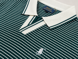 Close-up of a Polo Ralph Lauren knit polo shirt in dark green and white with a white collar, white embroidered polo player logo on the chest, and a blue brand label at the collar.