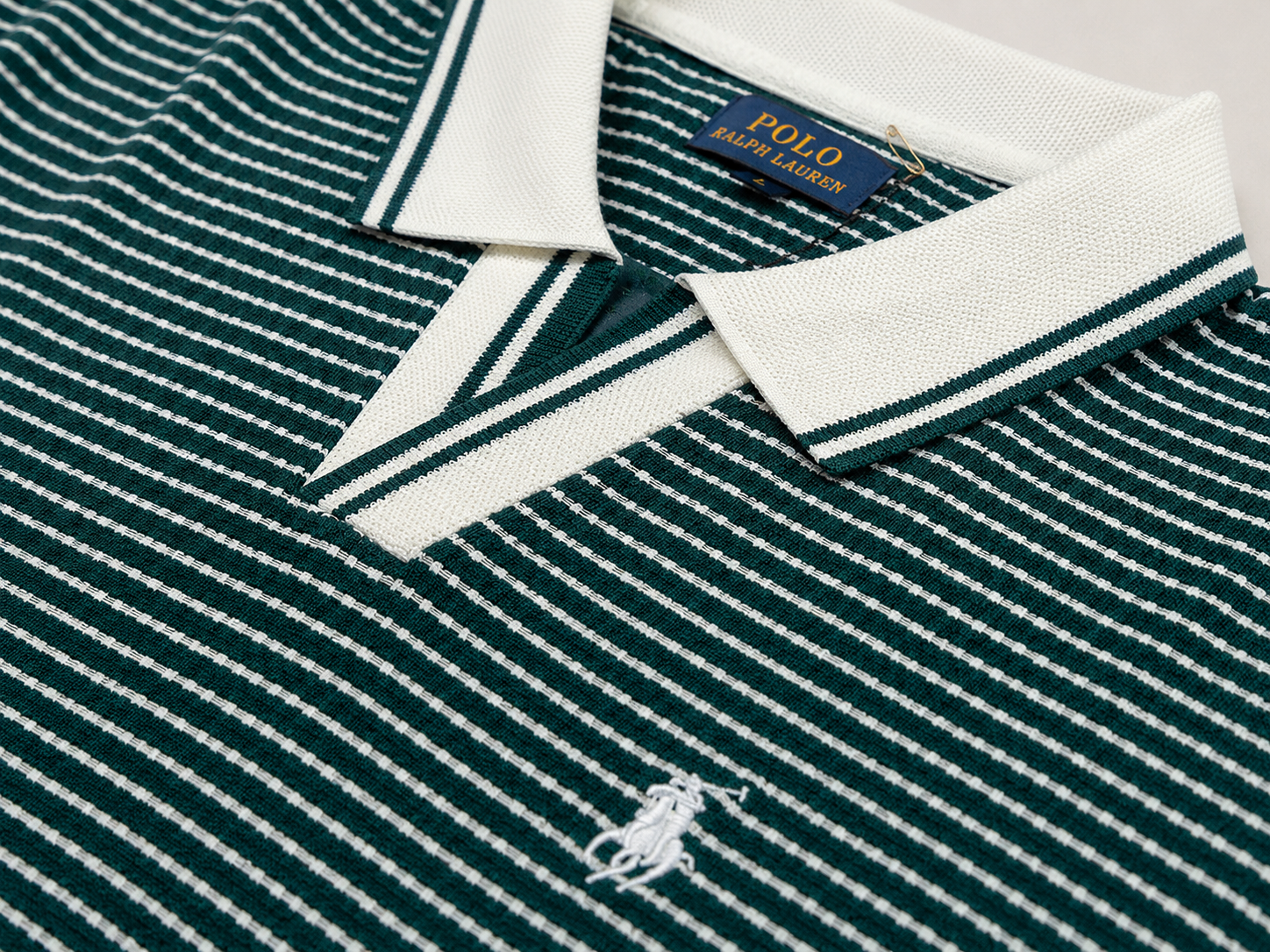 Close-up of a Polo Ralph Lauren knit polo shirt in dark green and white with a white collar, white embroidered polo player logo on the chest, and a blue brand label at the collar.