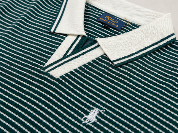 Close-up of a Polo Ralph Lauren knit polo shirt in dark green and white with a white collar, white embroidered polo player logo on the chest, and a blue brand label at the collar.