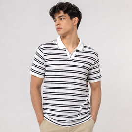 A man wearing a white short-sleeve polo shirt with thin black horizontal stripes and a small black embroidered polo player logo on the chest, paired with khaki pants, against a light gray studio background.