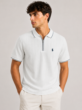 A man wearing a white short-sleeve polo shirt with thin navy blue piping and a small navy embroidered polo player logo on the chest, paired with light beige trousers, against a solid light gray background.
